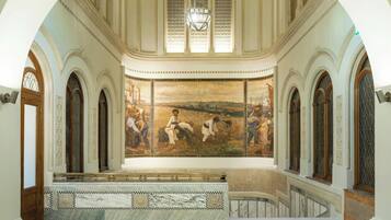 Un vaste hall doté d’un plafond haut, de fenêtres en arc de cercle et d’une fresque centrale représentant des scènes historiques.