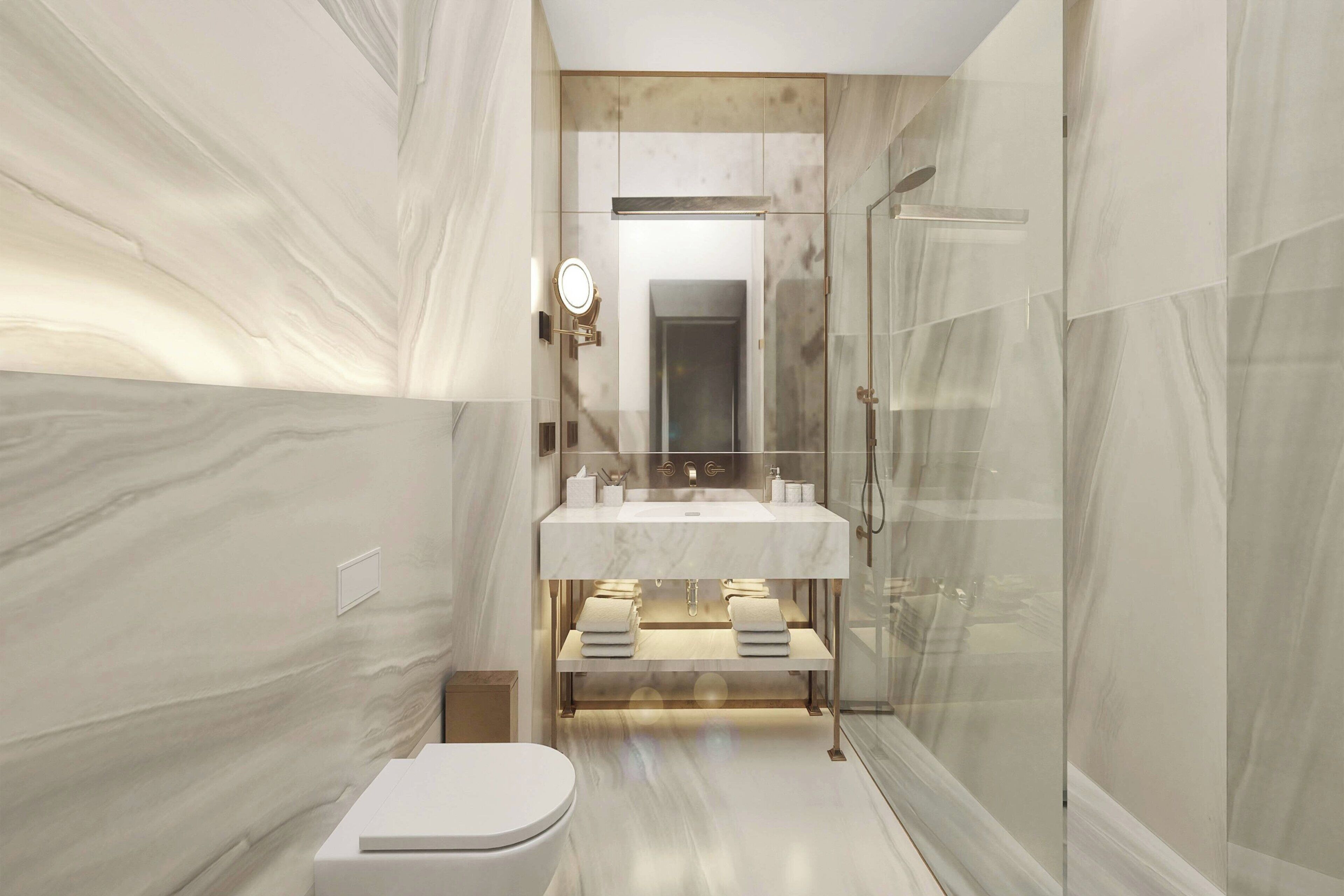 Un baño moderno con pared de mármol, lavamanos blanco, cabina de ducha con mampara de vidrio y un inodoro.