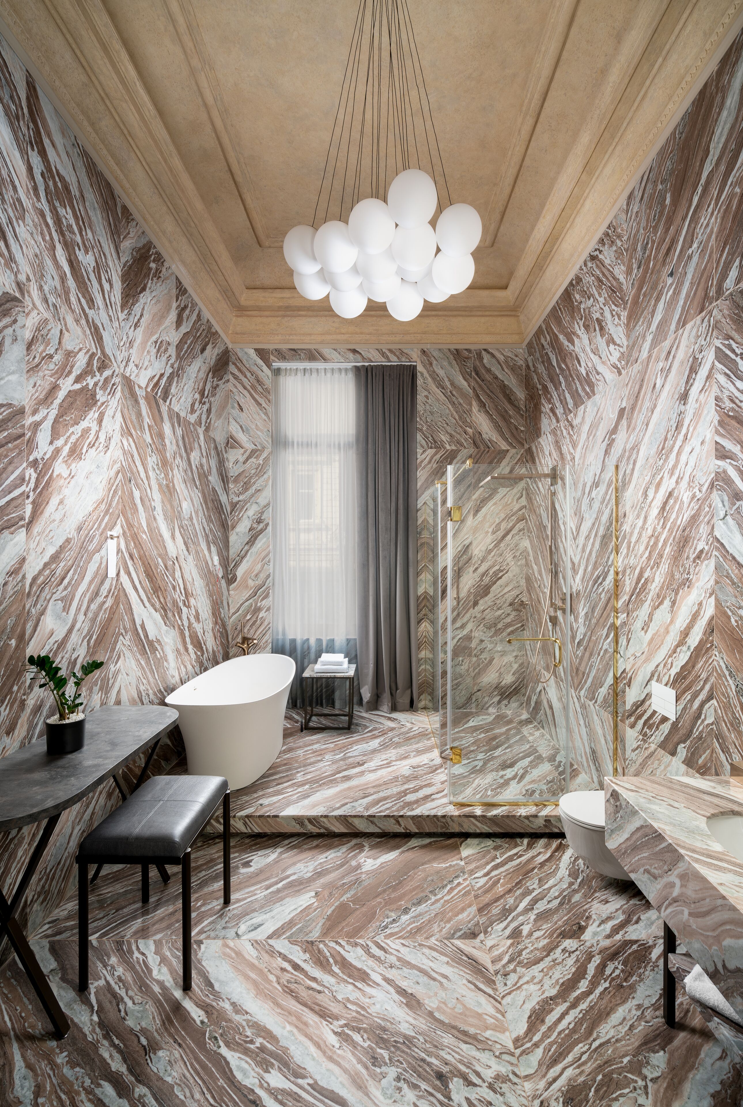 A bathroom with a freestanding bathtub, marble walls, and a modern chandelier.