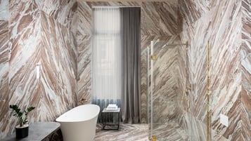 A bathroom with a freestanding bathtub, marble walls, and a modern chandelier.