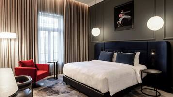 Et moderne hotelværelse med en stor seng, en rød lænestol, et rundt bord og et lille sofabord.