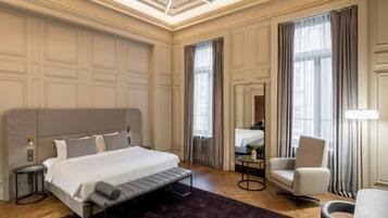 A modern hotel room with a large bed, a desk, a chair, and a large window with curtains.
