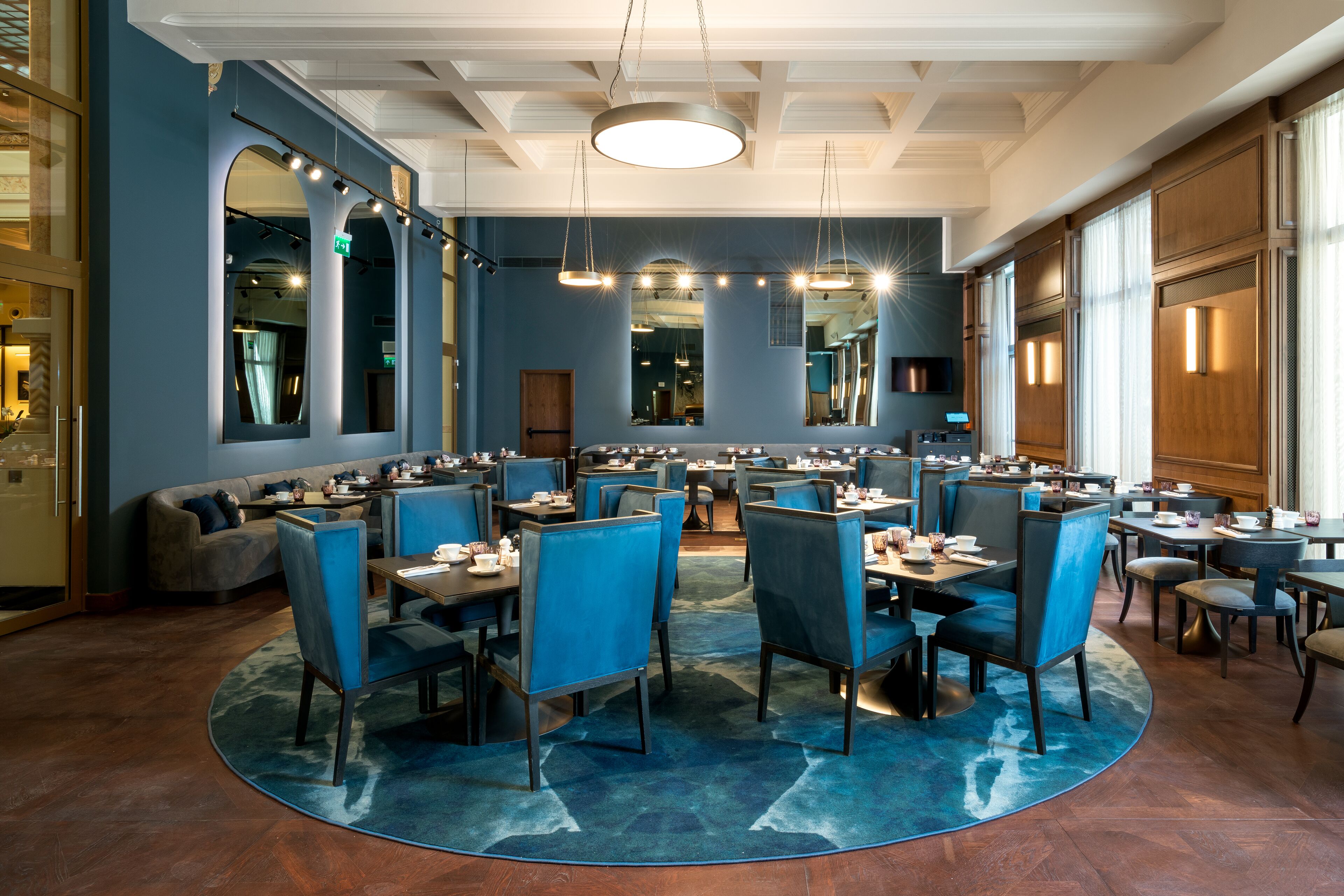 A spacious restaurant with high ceilings, blue walls, and a central round table surrounded by blue chairs.