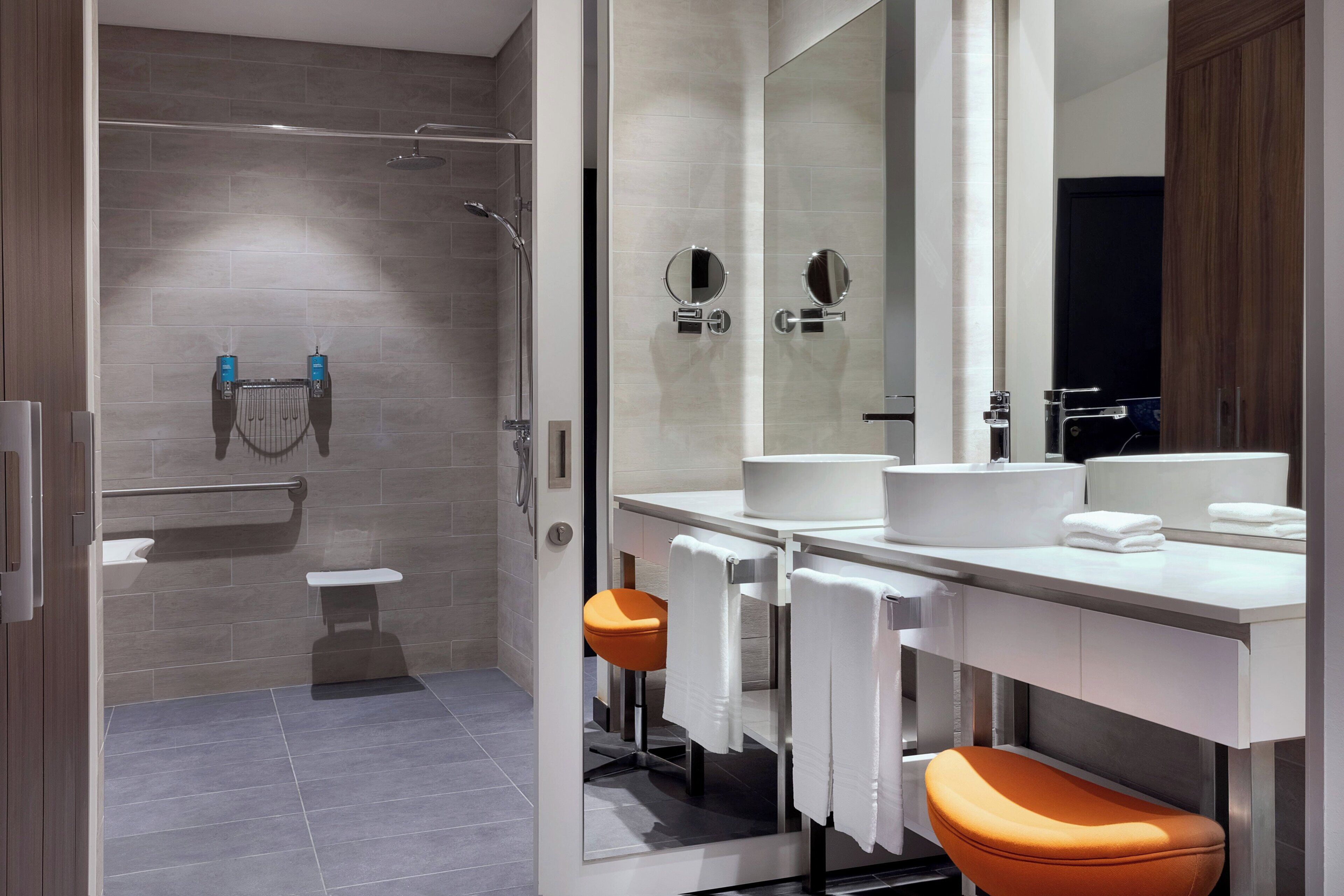 A modern bathroom with a glass shower enclosure, a white sink, and an orange stool.