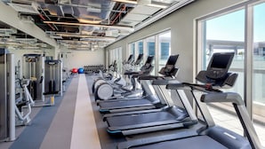 Une salle de sport moderne équipée de tapis de course, de vélos elliptiques et de poids libres.