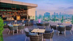 Un bar situé sur un toit, avec des chaises en osier et un comptoir, offrant une vue panoramique sur la ville.