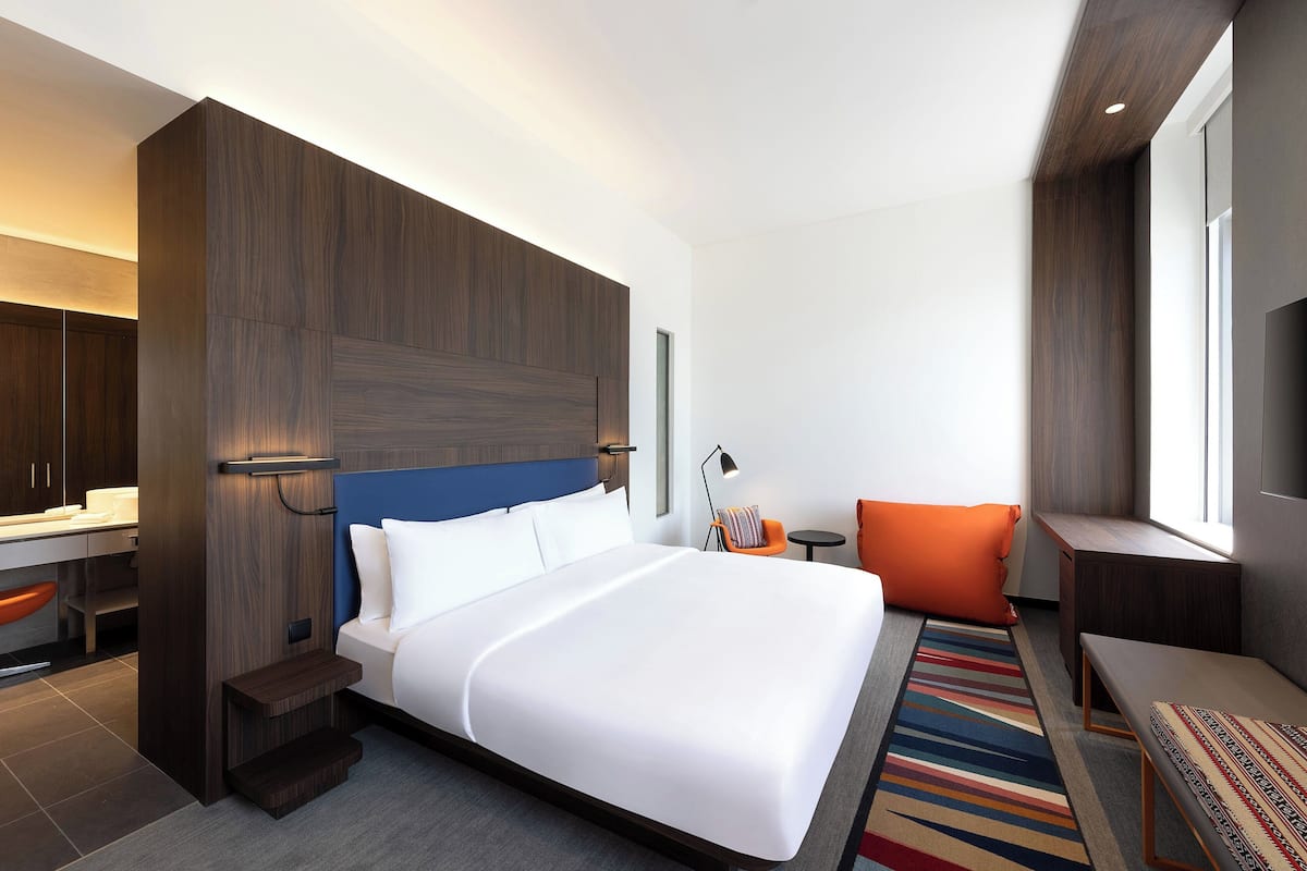 A modern hotel room with a large bed, a desk, and a seating area.