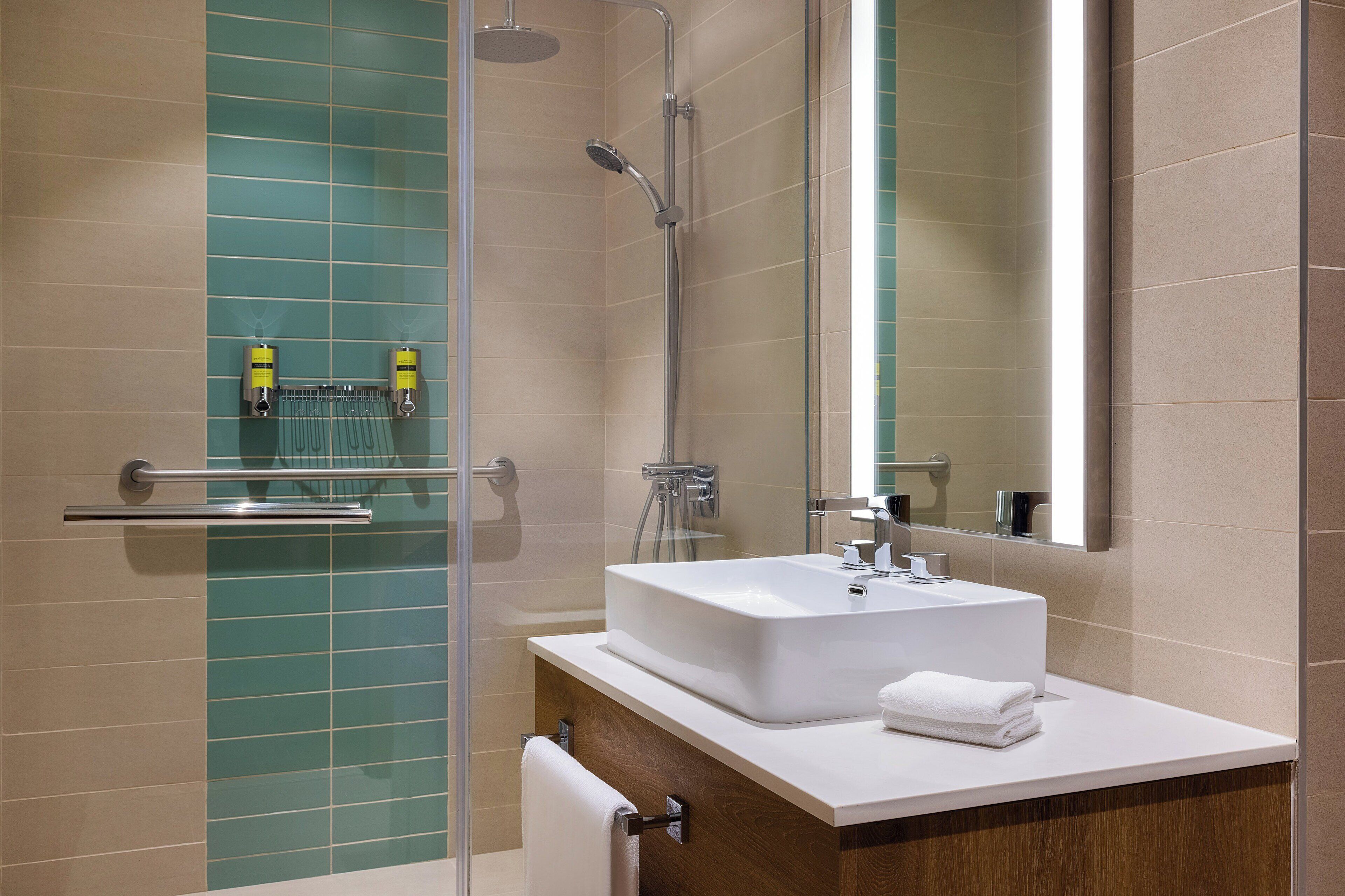 A modern bathroom with a glass shower enclosure, a white sink, and a large mirror.