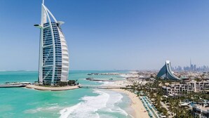 A coastal cityscape with a prominent modern tower and a curved building near a beach. - Element by Marriott Al Mina, Dubai (Dubai)