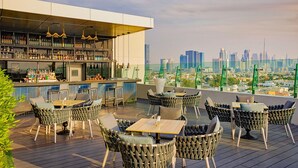 A rooftop bar with wicker chairs and a bar stocked with bottles, overlooking a city skyline. - Element by Marriott Al Mina, Dubai (Dubai)