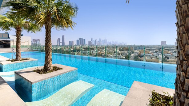 A rooftop infinity pool with clear blue water, palm trees, and a city skyline in the background. - Element by Marriott Al Mina, Dubai (Dubai)