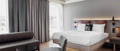 Une chambre d’hôtel moderne avec un grand lit, un canapé, un fauteuil et une petite table.
