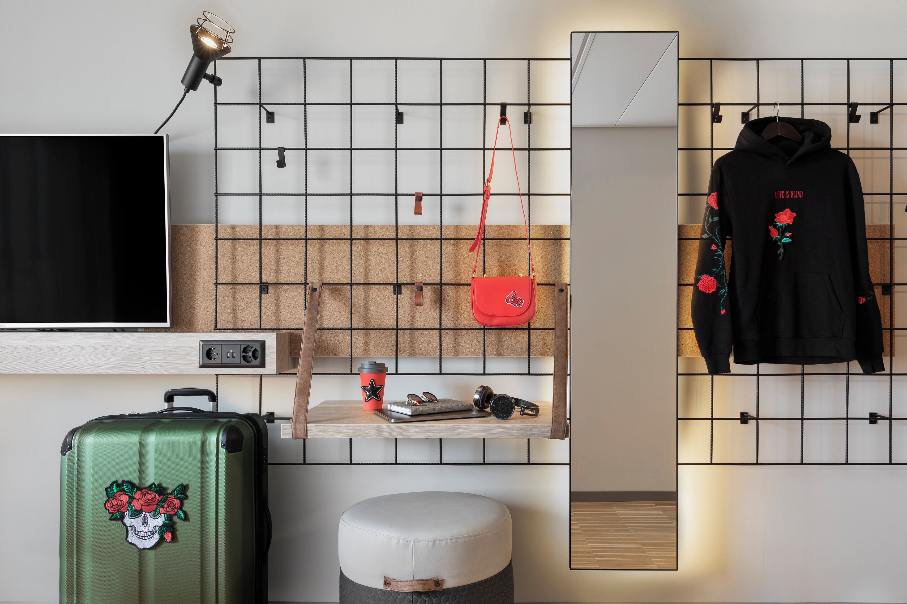 Een moderne kamer met een televisie, een groene koffer, een rode tas, een zwarte hoodie en een houten plank met diverse spullen.
