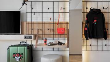 Een moderne kamer met een televisie, een groene koffer, een rode tas, een zwarte hoodie en een houten plank met diverse spullen.