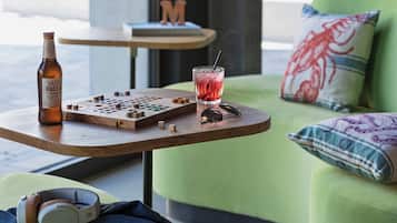 Una mesa de madera con una botella de Vadia Pale Ale, un tablero de ajedrez y una copa de bebida roja.
