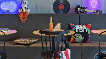 Un área de descanso moderna con un sofá, dos mesas redondas pequeñas, una decoración con forma de cohete, un disco de vinilo, una guitarra y un letrero de neón.