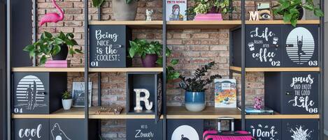 Una pared con estantes que exhiben varios objetos decorativos, como plantas en macetas, citas enmarcadas y una maleta rosa.