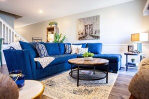 A modern living room with a blue sofa, a round coffee table, and a painting on the wall.
