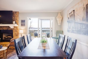 Une salle à manger avec une longue table, des chaises, une cheminée, un téléviseur et une vue sur l’extérieur.