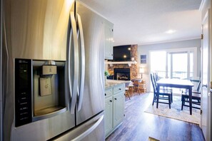 A modern kitchen with stainless steel appliances, a stone fireplace, and a dining area with a table and chairs.