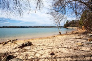 A beach with clear water, rocky shoreline, and sparse vegetation.