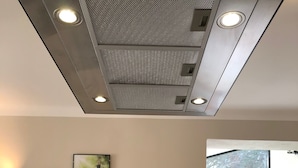 Eine moderne Küche mit integriertem Spülbecken, einem Edelstahlarmaturen und einer Spritzschutzleiste mit geometrischem Muster. Ein Gemälde hängt an der Wand und ein Fenster lässt Tageslicht herein.