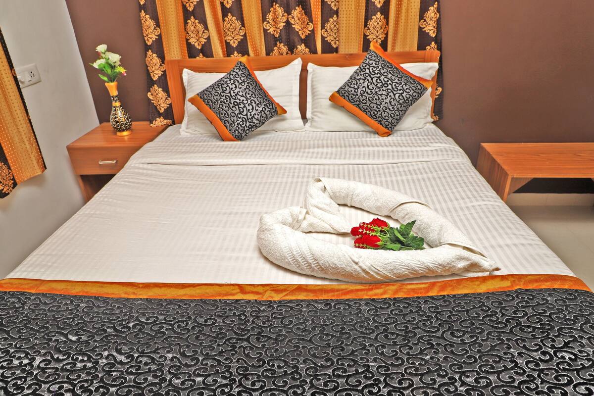 Un lit bien fait, agrémenté d’un coussin décoratif, d’un vase de fleurs et d’une serviette ornée d’une rose.