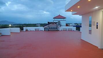 A rooftop terrace with a red floor, a covered seating area, and a view of distant buildings and mountains.