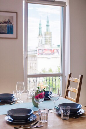 Une table à manger dressée avec des assiettes, des verres et des couverts, donnant sur un paysage urbain dominé par une tour imposante.
