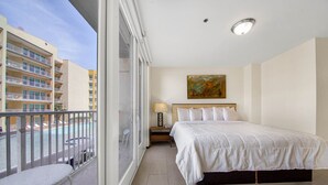 A hotel room with a balcony, a bed, a nightstand, and a painting on the wall. - Lovely One Bedroom Unit on SPI + Infinity Pool (South Padre Island)