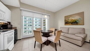 A modern kitchen with white cabinets, a dining area with a round table and wicker chairs, a beige sofa, and a large abstract painting on the wall.