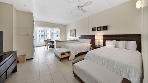 A hotel room with two beds, a desk, a chair, a TV, and a ceiling fan.