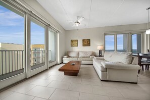 A spacious living room with a large sliding glass door, a ceiling fan, a wooden coffee table, and a beige sofa. - Two Bedroom Apt on Tropical Paradise SPI (South Padre Island)