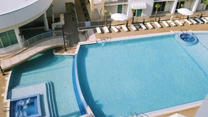 A large outdoor swimming pool with a separate hot tub area, surrounded by lounge chairs and umbrellas.