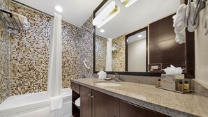 A modern bathroom with a mosaic tile shower wall, a large mirror, and a granite countertop.
