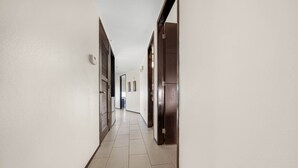 A long, narrow hallway with white walls and a tiled floor, leading to a door at the end. - Wonderful Three Bedroom Condo Partial Ocean Views (South Padre Island)