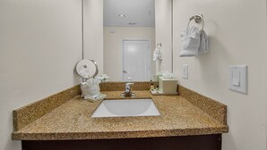 A bathroom with a granite countertop, a sink, a mirror, a towel rack, and a door.