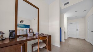 A hotel room with a wooden desk, a chair, a large mirror, and a door leading to another room.