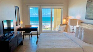 A hotel room with a bed, a desk, a chair, a TV, and a balcony with a view of the sea. - Perfect Fully Furnished 3Bedroom Condo Ocean View  (South Padre Island)