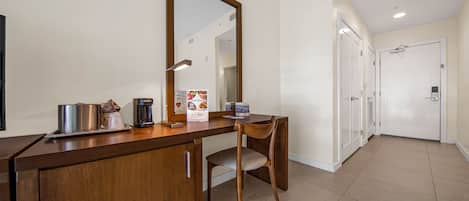 Una habitación de hotel con un escritorio de madera, una silla, cafetera y un espejo.