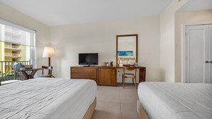 A hotel room with two beds, a desk with a chair, a television, and a window with a balcony view.