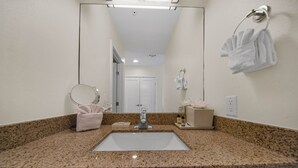 A bathroom with a granite countertop, a sink, a mirror, a towel rack, and a door in the background.
