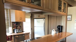 Une cuisine avec des meubles de rangement en bois, un réfrigérateur en acier inoxydable, un comptoir-bar en bois avec des tabourets et une machine à café.