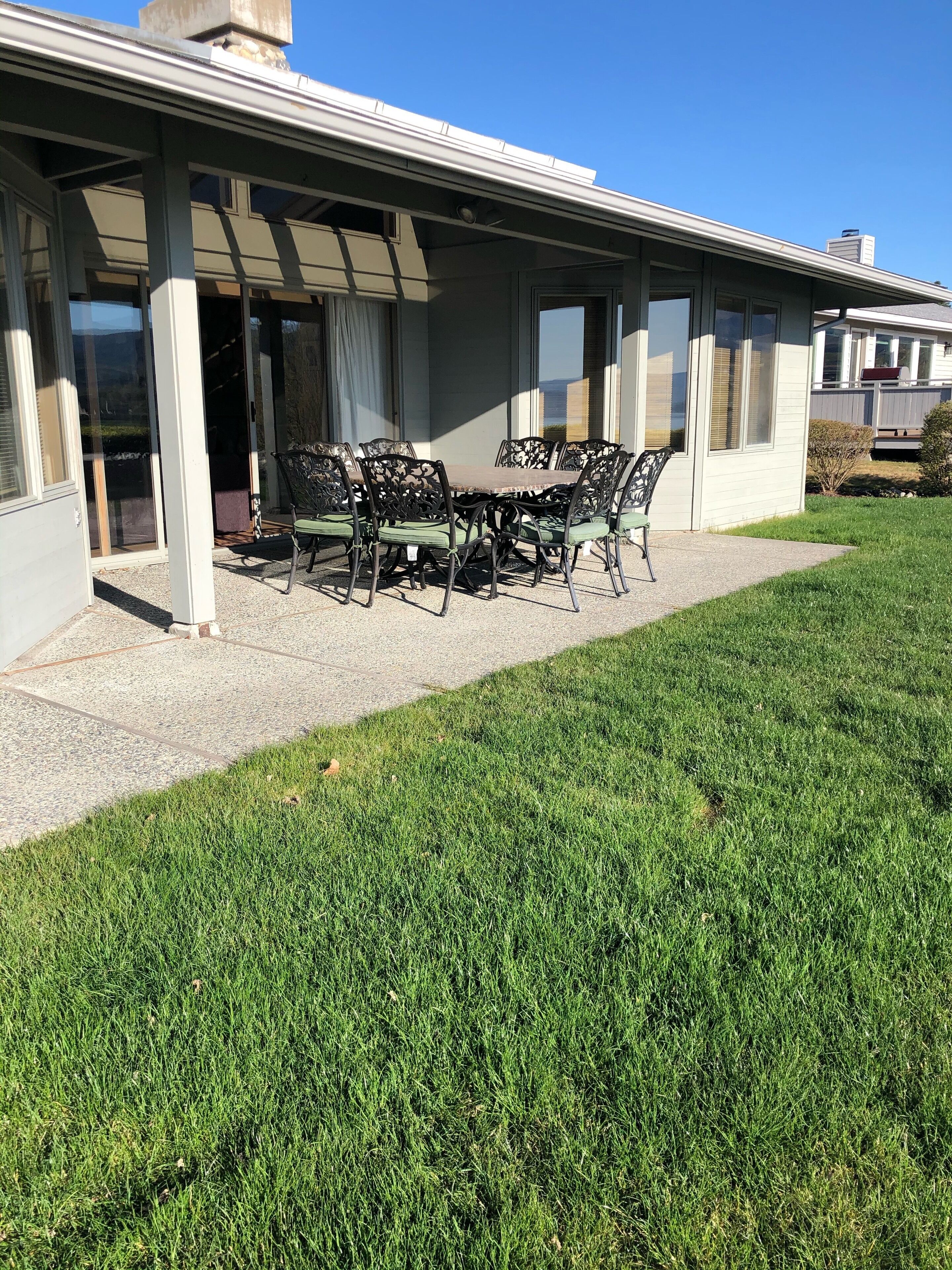 A covered patio area with a table and chairs, a grassy lawn, and a building with large windows and a chimney.