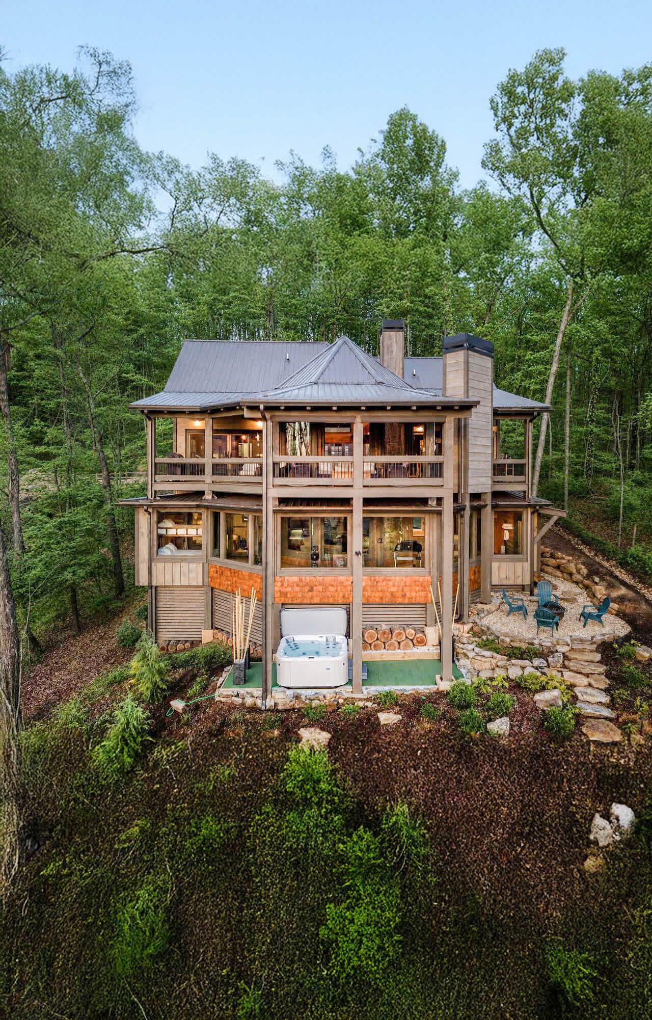A multi-level cabin with a deck and outdoor seating area surrounded by forest.