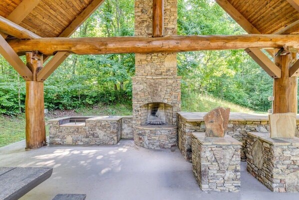A stone fireplace with a chimney, surrounded by stone benches and a wooden table.