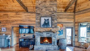 A log cabin interior with a stone fireplace, a bear painting, a television, and a rustic dining area. - The Secret of Blue Ridge, SHHHH don't tell anyone! (Cherry Log)