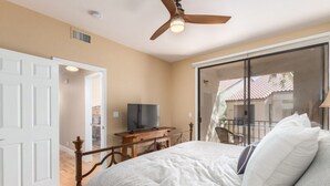 Una camera da letto con un letto, una televisione su un tavolino in legno e una porta scorrevole in vetro che dà su un balcone.