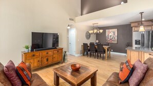 Un ampio soggiorno con una grande TV a schermo piatto, mobili in legno e una zona pranzo con sedie e tavolo.