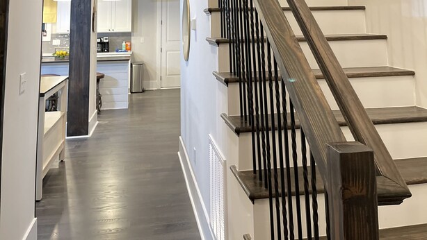 Ein modernes Interieur mit einer Holztreppe, einem 'WELCOME'-Schild und einem durch einen offenen Durchgang einsehbarer Küchenbereich.